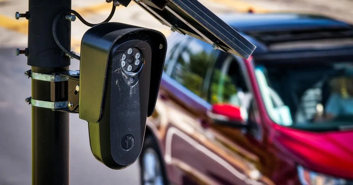 A Flock automated license plate reader mounted on a pole near a roadway